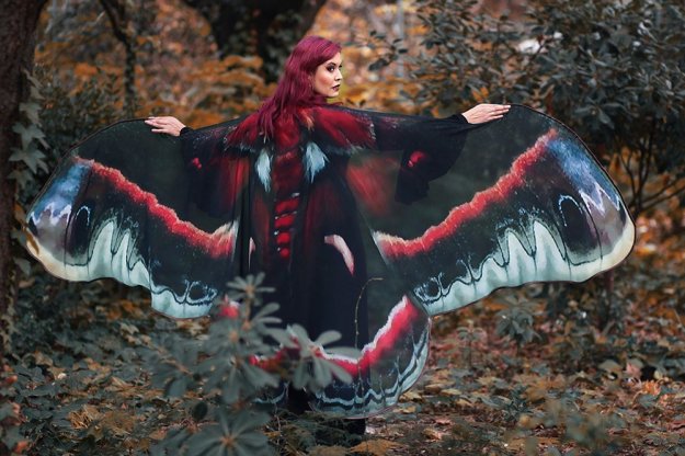 Person wearing a black, white, and crimson cape patterned like moth wings. Cape is wider than armspan in width, makeing the wearer appear to have moth wings.